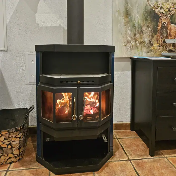 ein schwarzer, angezündeter Ofen links vor einem Bild mit einem Hirsch