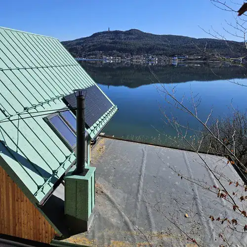 Kaminbau ein schwarzer Kamin vor grünem Dach und See
