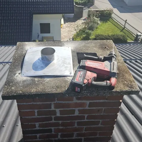 Quadrat_Kamin mit Werkzeug Silberner Kamin mit rot schwarzem Werkzeug darauf liegend