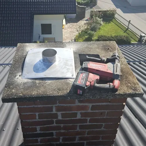 Quadrat_Kamin mit Werkzeug Silberner Kamin mit rot schwarzem Werkzeug darauf liegend